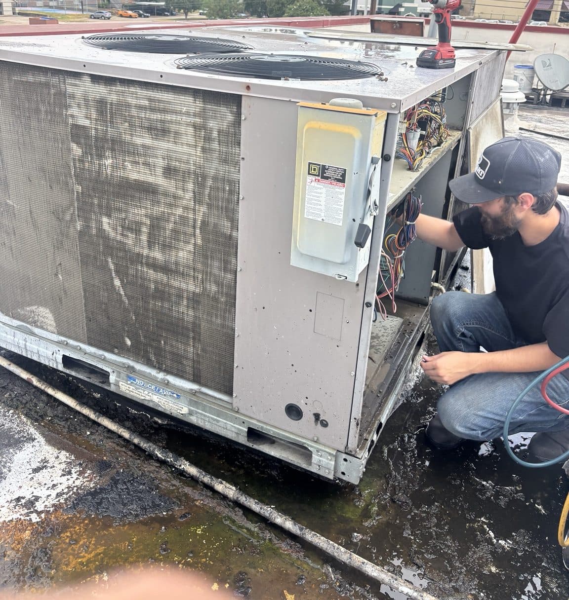 Technician working inside a commercial rooftop HVAC unit's control panel