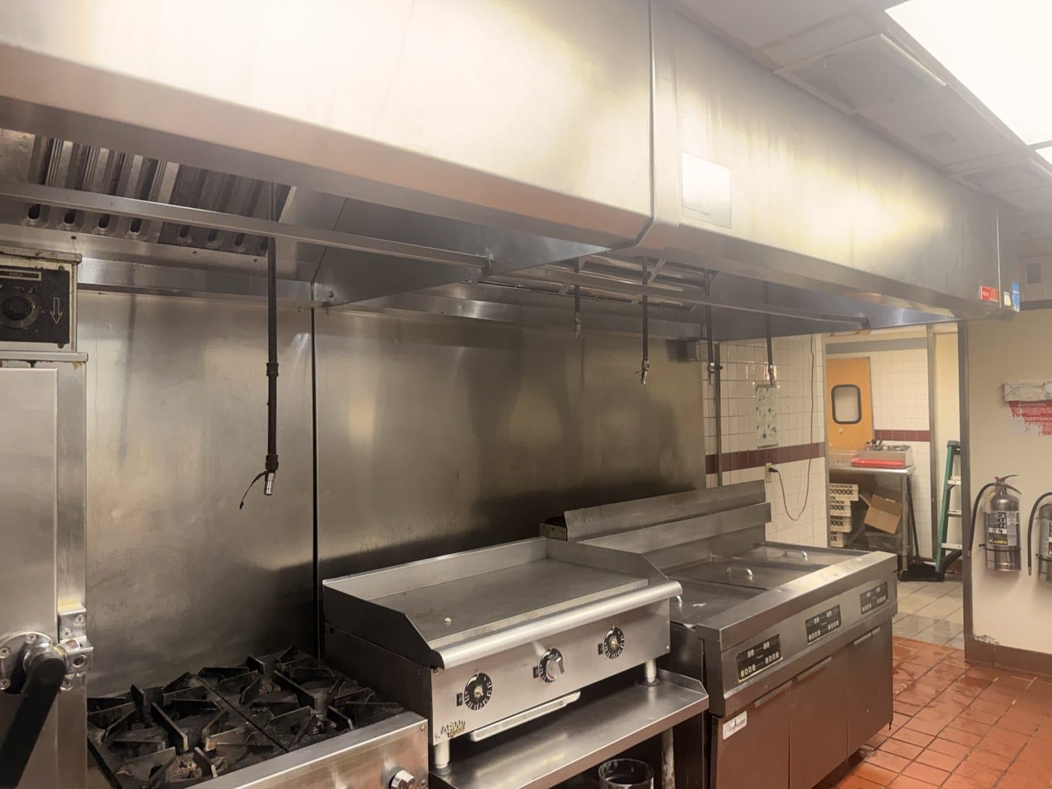 Cleaned commercial kitchen exhaust hood above a griddle and range